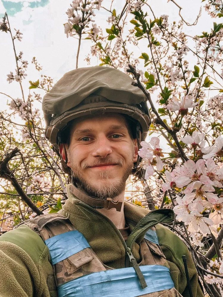 Усміхнений Дмитро Козацький у шоломі й бронежилеті серед квітучих дерев